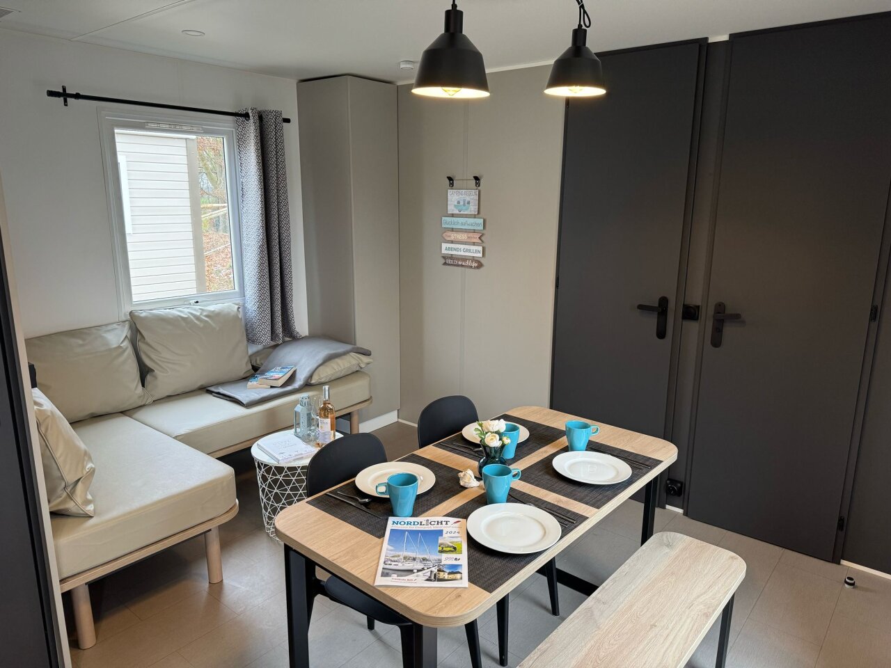 Gemütlicher Wohnbereich im Mobilheim/ Chalet mit Sofa, Fernseher und direktem Zugang zur Terrasse.